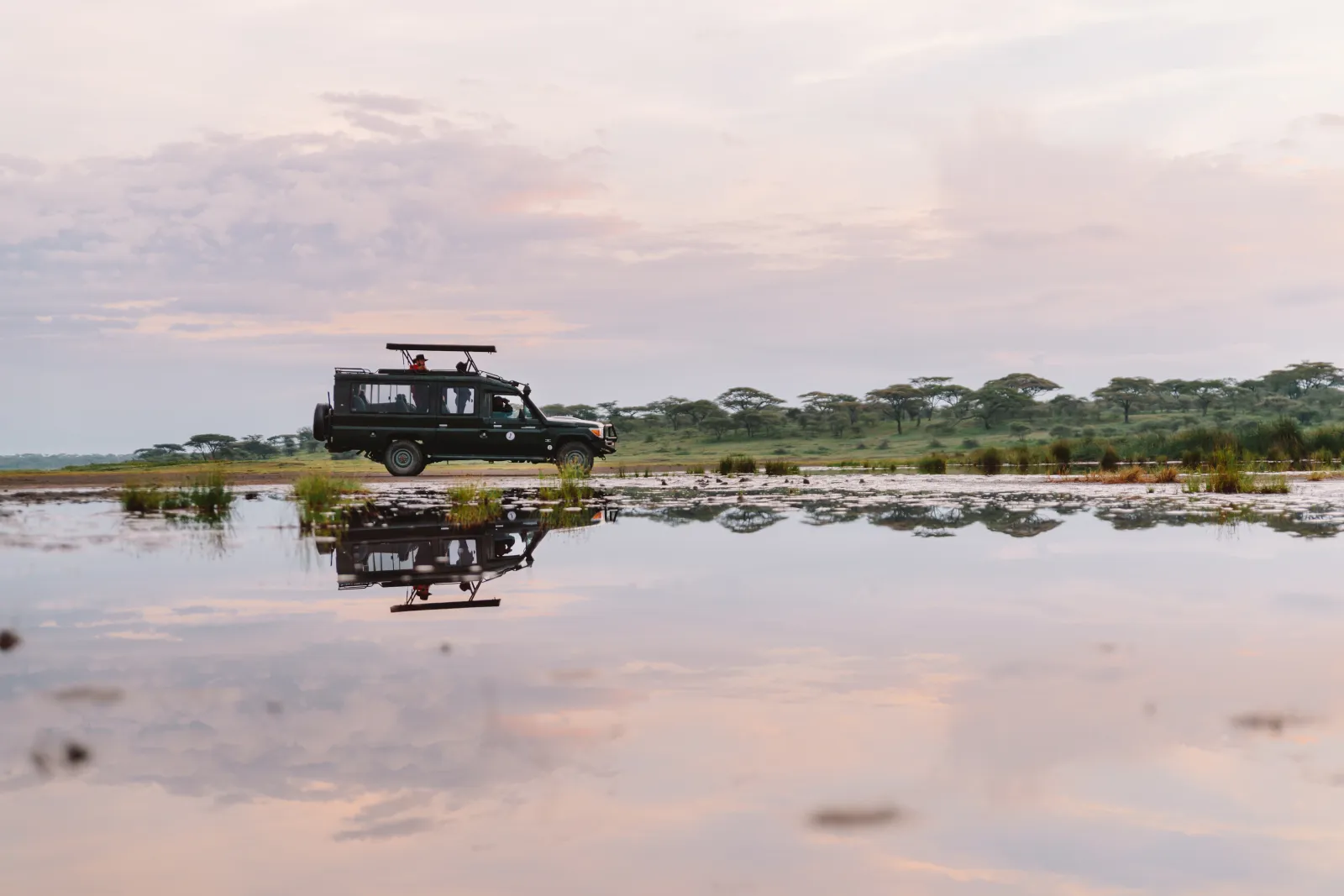 A game drive vehicle reflected in still water at first light